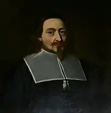 A head and shoulders portrait of Endecott. He wears a black magistrate's robe, with a falling collar or clerical rabat of gray. He has a narrow goatee beard and a moustache that roughly form a cross.