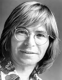 A smiling man with long fair hair wearing glasses