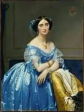 Princess Albert de Broglie wears a blue silk evening gown with delicate lace and ribbon trim. Her hair is covered with a sheer frill trimmed with matching blue ribbon knots. She wears a necklace, tasseled earrings and bracelets on each wrist.