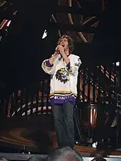 A young man wearing jeans and a hockey jersey singing into a microphone on stage