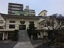 View of steps leading up to two story temple with city skyline in background.