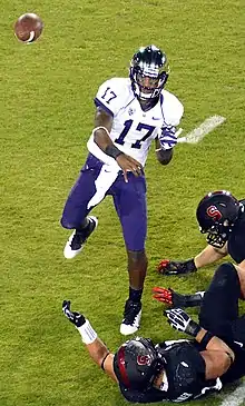 An African-American man wearing a white football jersey emblazoned with number 17 and purple pants throws a pass; the hands of various defenders are visible.