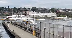 This picture shows the passenger loading area at the Kenmore Air Harbor Seaplane Base in Seattle, USA. Three planes are at the dock while one plane is taxiing in the waters of Lake Union.