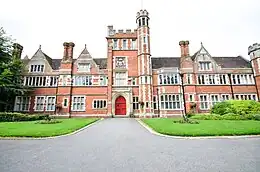 A mock tudor, red brick building with crenellations in white stone and a central tower.