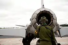  Headphone-wearing technician in green uniform, inspecting the engine nozzle of a single-engine fighter jet