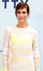 A brunette woman wearing a white dress with some lace detailing smiles