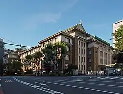 Across this street is a large five story brick building with several sloped Japanese green tiled roofs