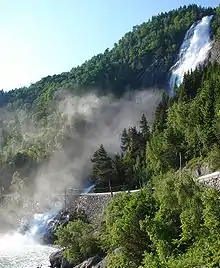 A waterfall on a wooded hill next to a road