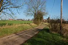 A country lane with three buildings on the horizon