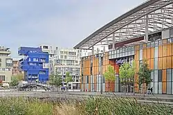 A large building faced with panels of wood and glass, and an arched roof, labelled "Confluence", is on the right.  Other modern city buildings are across a bridge, on the left of the frame.