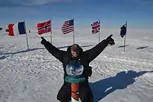 A man posing at the indication of the South Pole, with flags of the countries that have visited it