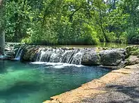 Small waterfall along a river's path with trees shading it