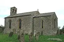 A small, simple stone church.  On the left is the nave with a bellcote at the far end, and on the right a smaller chancel