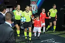 some football referees lead some mascots through a tunnel at a big club football match