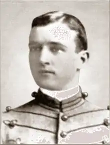 Head of a young white man with neatly combed hair wearing a jacket with lines of decorative piping running horizontally across the chest.