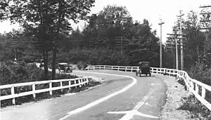 A grayscale view of a rural two-lane road lined with fences and telephone poles