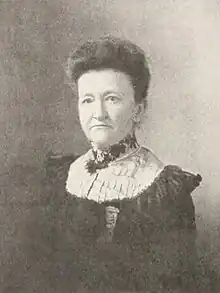 B&W portrait photo of a middle-aged woman with dark hair in an up-do wearing a dark blouse with white lace detail