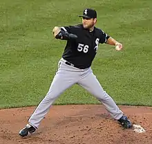 A man in a black baseball jersey, gray pants, and black cap