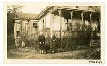 A sepia toned photograph of two older women and a black dog on a gravel pathway. There is a large house (Point Ellice House) behind them. A large lawn occupies the left side of the photograph.