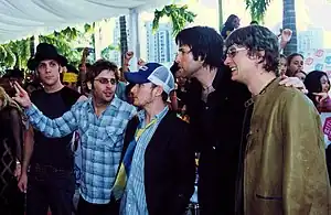 A group of five young men wearing casual clothing standing together, some with their arms round each other's shoulders