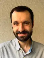 A man with dark hair and a dark beard smiling at the camera.