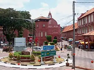 Town scene with three-storied red houses and a red church. There is a three-storied clock tower standing on a square.