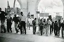 Men march up the Frary Dining Hall steps carrying handwritten protest signs