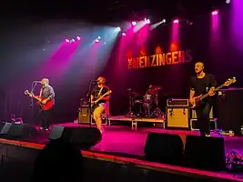 The four members playing on a red light cast stage.