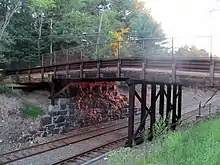 A wooden bridge with one stone abutment over a railway line