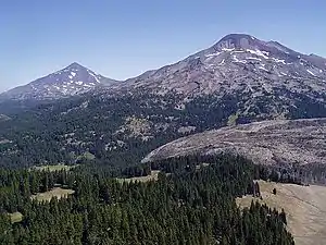 An aerial image displays Middle Sister on the left and South Sister to the right above the vegetation of the Three Sisters Wilderness.