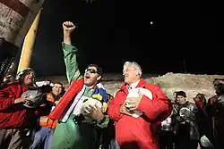 Color image of the mining leader and the Chilean President leading rescue workers in a rendition of the Chilean anthem.