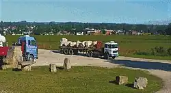 A dump truck carrying large rocks from a local quarry, with the city of Batán in the background