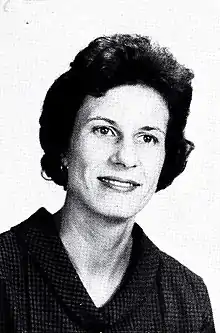 Black and white head an shoulders image of a short-haired woman wearing a v-necked dark blouse and small pearl earrings.