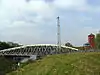 A metal swing bridge on the left over the canal, a metal pylon in the middle and brick support buildings on the right.