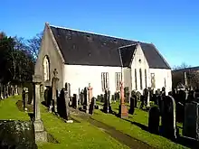 An image of an old, cream coloured church building. In the foreground are an array of gravestones and memorials.