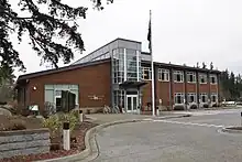 A brown building with two stories, a large glass atrium, and a flagpole.