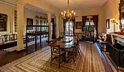 A dining room with a table and chairs in the center and a chandelier above them