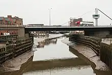 The bridge in its closed position with road traffic traversing it. The river below is at low water and shows the wooden piling in the river to protect the bridge