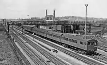 A black and white image of an electric multiple unit on the furthest of four tracks.