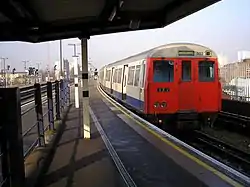 A grey, red and blue A Stock Stock East London Line train waiting to depart New Cross Station for Whitechapel.