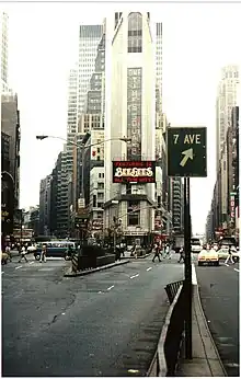 The northern facade of One Times Square as viewed from 45th Street in 1977. Broadway is to the left, and Seventh Avenue is to the right. A sign, pointing motorists toward Seventh Avenue, is visible in the foreground.