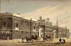 Engraving of large dark stone-block building, with horse-drawn carriages in the street in front