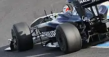 a navy open wheeled racing car drives on a tarmac course