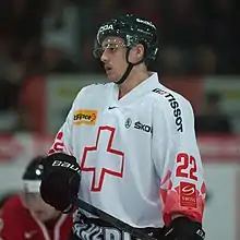 A Caucasian male ice hockey player shown from the knees up. He is wearing a red and white sweater with a black helmet.