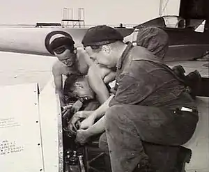 Three men in overalls working on an aircraft engine