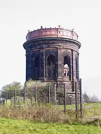 A circular stone tower with pilasters and arches, carrying an iron tank