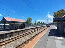 Electric multiple unit train arriving at a bitumen train platform. The platform has a small shelter on it.