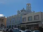 Front facade has balustrade parapet and cornice. Hood moulds plus panels to first floor windows. Plastered ashlar below. Fine 1880s facade. Complex building behind. This building is unique in structure and was used by Henry Carter Galpin, watchmaker and jeweller, as a home and business premises soon after his arrival in Grahamstown in 1849. In 1880 Galpin installed a camera obscura in the turret of the building. Current use: Commercial – Observatory.  This building is unique in structure and was used by Henry Carter Galpin, watchmaker and jeweller, as a home and business premises soon after his arrival in Grahamstown in 1849. In 1880 Galpin installed a camera obscura in the turret of the building.