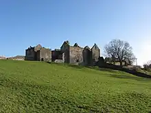 roofless stone buildings at the top of a grass covered hill