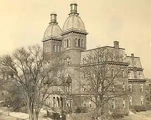 A 4-story building with two identical towers at the top surrounded by leafless trees